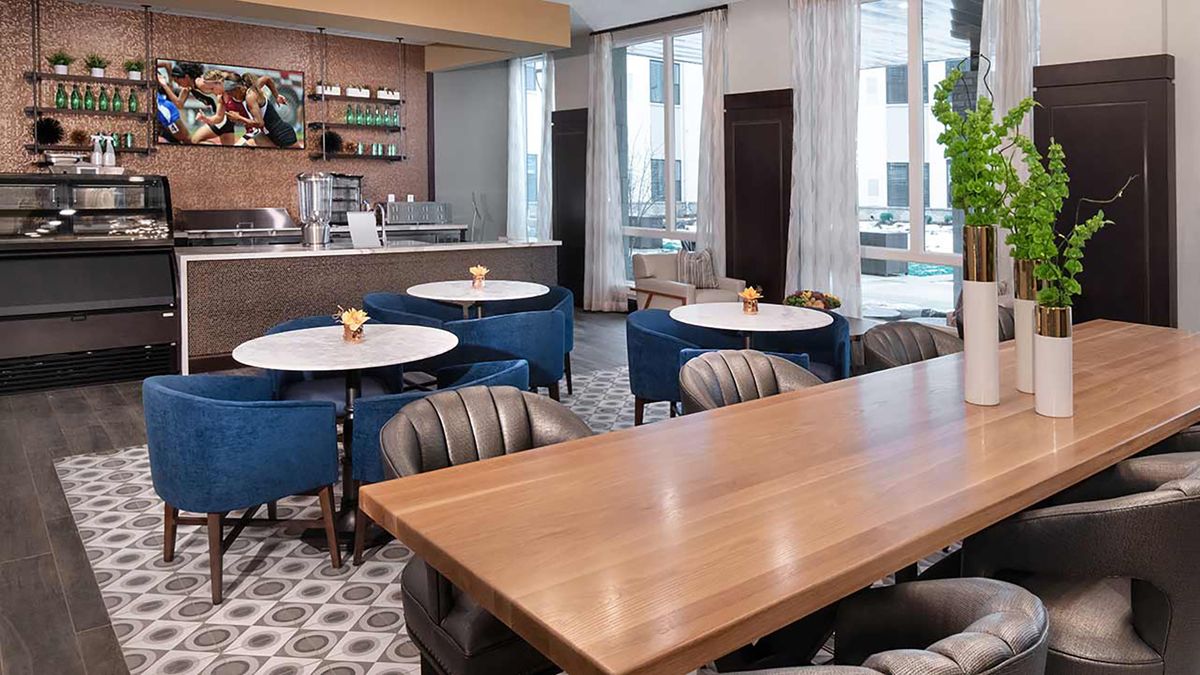A modern and stylish cafe interior with a mix of round and rectangular tables, comfortable seating, and a coffee bar backdrop.