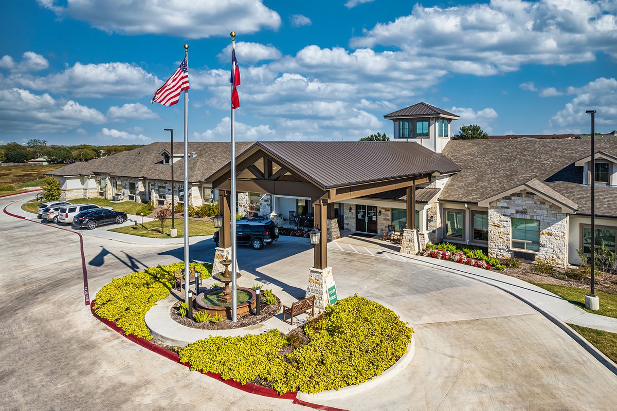 A building entrance with flags and neatly arranged landscaping under a partly cloudy sky.