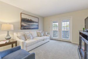 A cozy living room with a white sofa, decorative pillows, and artwork on the wall, illuminated by natural light from French doors.