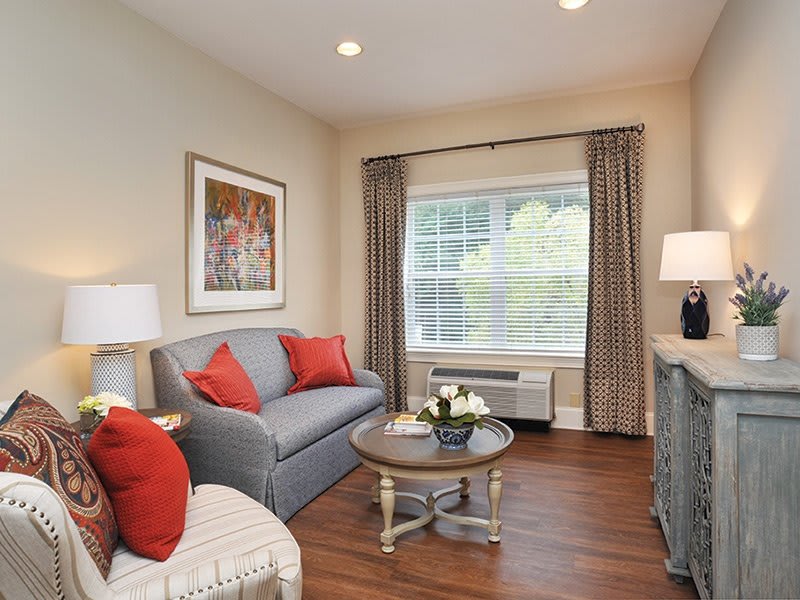 A cozy living room with a gray sofa, red cushions, and a coffee table set in front of a large window.