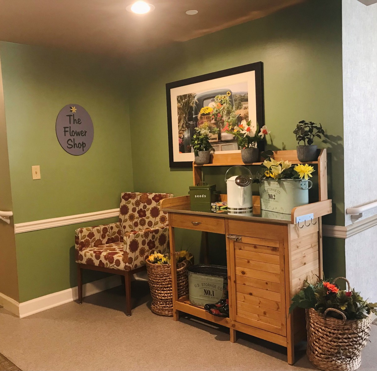 A cozy corner with green walls, featuring a patterned chair, a wooden table adorned with flowers and decorative items, and a picture on the wall.