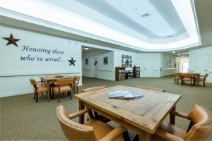 A spacious and well-lit community lounge area with tables, chairs, and wall decorations.