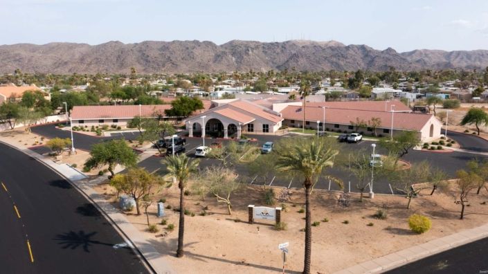 A desert landscape with a building, surrounded by mountains and palm trees.