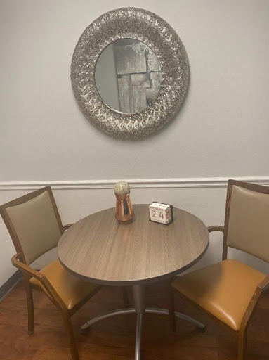 A cozy dining setup featuring a round table and two chairs beneath a decorative mirror.