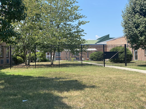 A fenced area with well-maintained grass and trees under a clear blue sky.