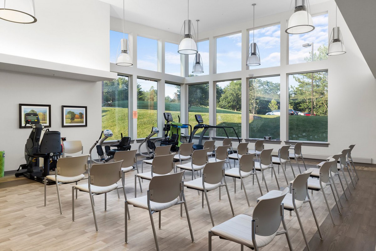 A bright, modern meeting room with rows of chairs and large windows overlooking greenery.