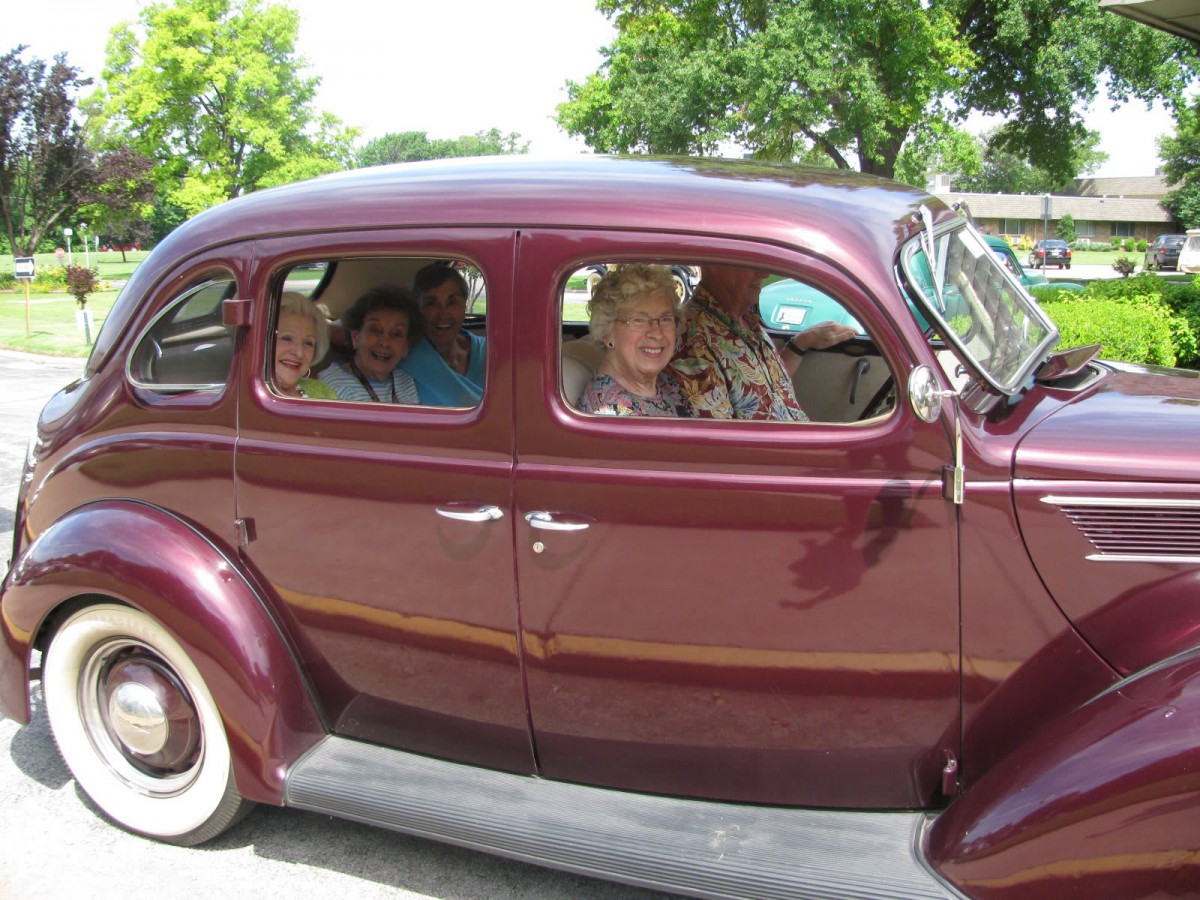 A group of people sitting inside a vintage maroon car parked outdoors.