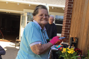 An elderly woman happily gardening outdoors, wearing gloves and tending to flowers.