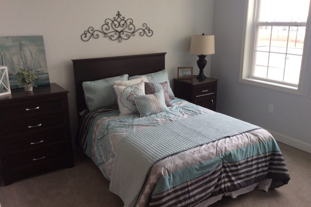 A neatly arranged bedroom with a bed, decorative pillows, and a lamp on the nightstand.