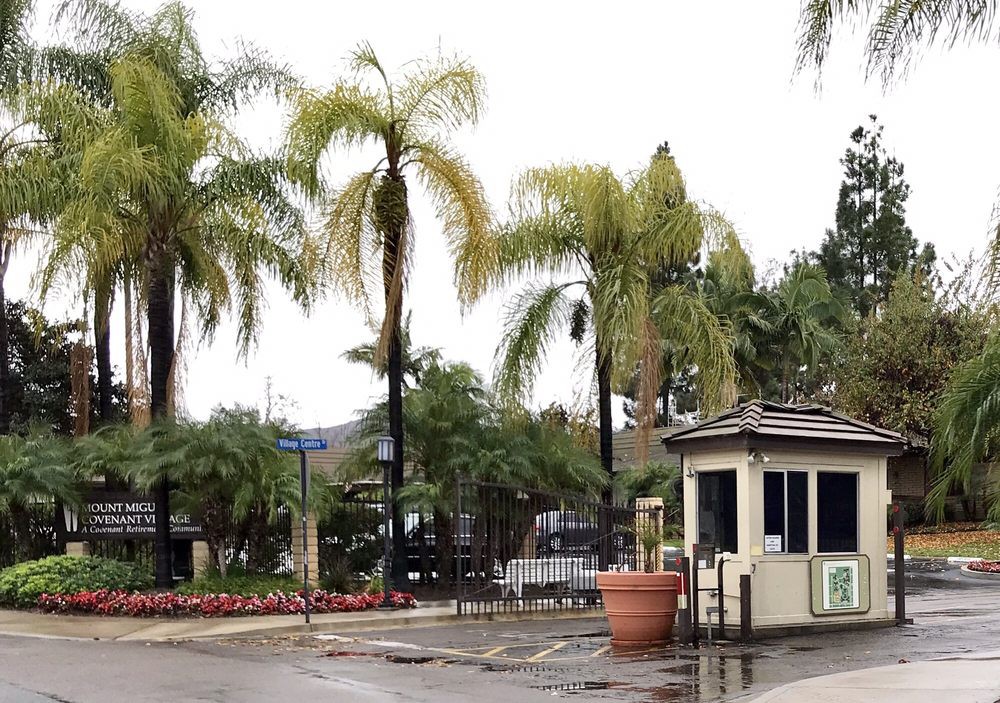 A rainy day view of an entrance with palm trees and a guardhouse.