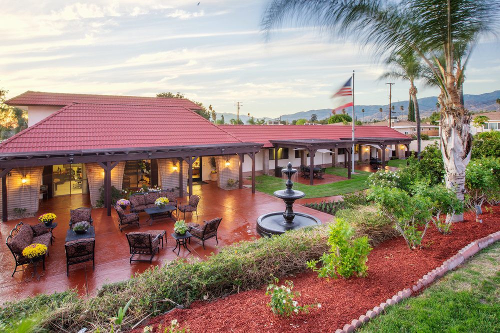 A spacious outdoor patio area with seating arrangements, a fountain, and well-maintained gardens under a clear sky.
