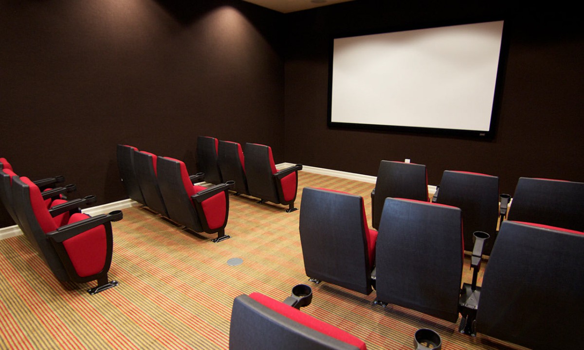 An empty home theater room with rows of red and black seats facing a projector screen.