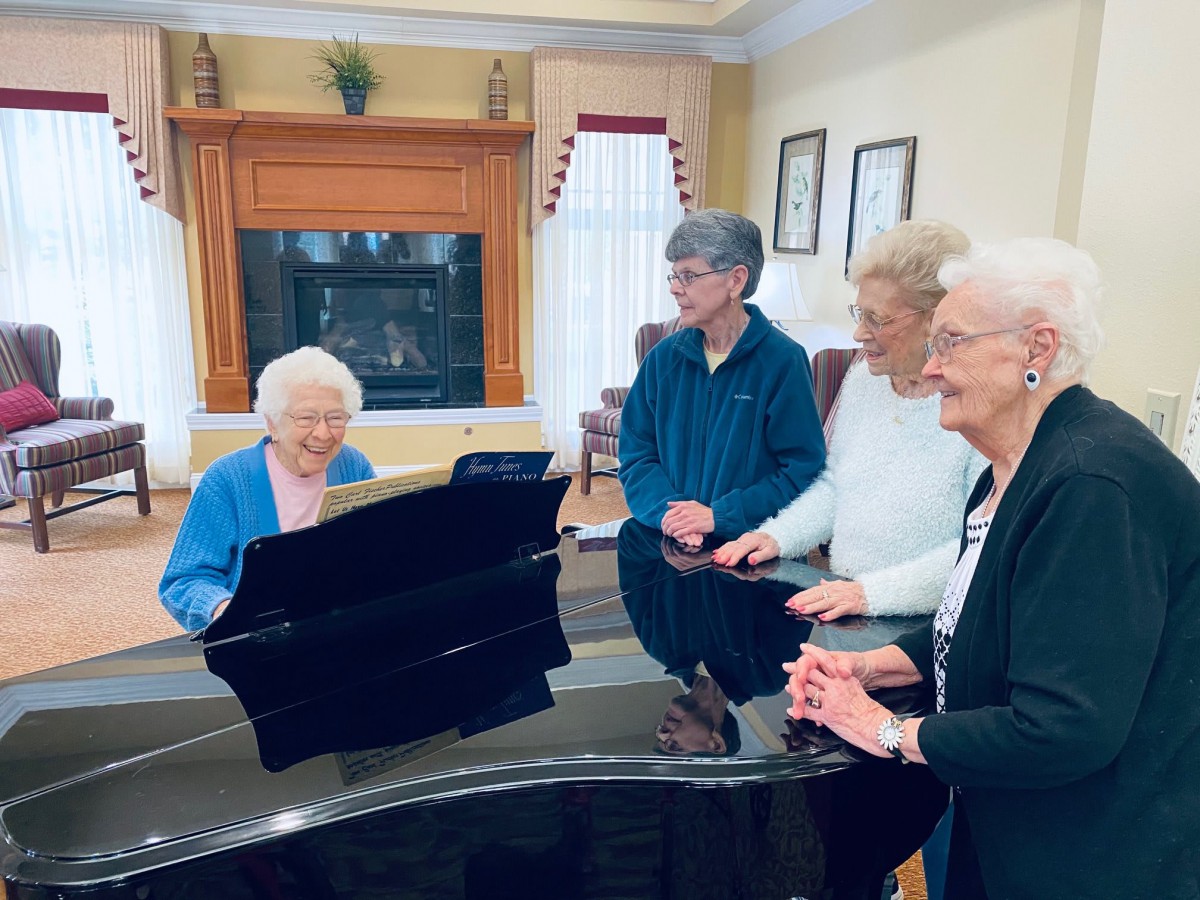 A group of elderly individuals enjoying a musical moment around a piano.