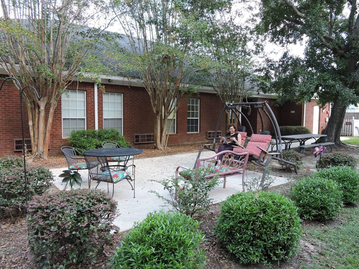 A cozy patio area with outdoor furniture surrounded by trees and bushes next to a brick building.