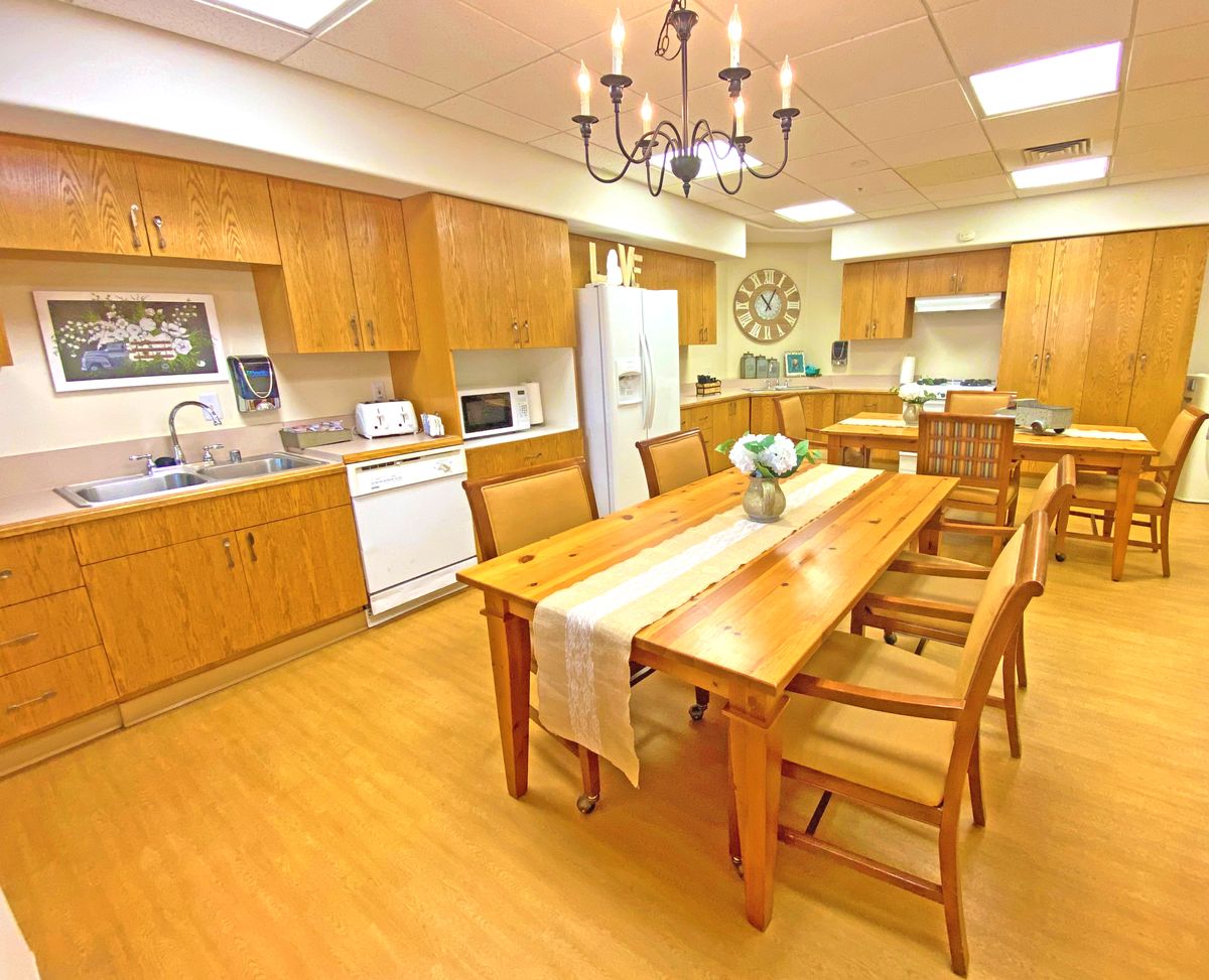 A spacious kitchen with wooden cabinetry and a large dining table under a chandelier.