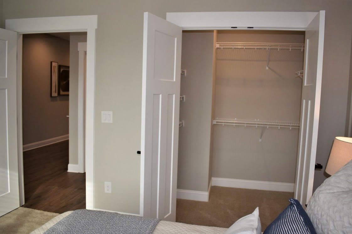 A bedroom interior featuring an open closet with shelving and a partially visible bed.