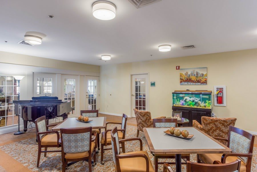 A well-lit interior room featuring tables, chairs, an aquarium, and a piano.