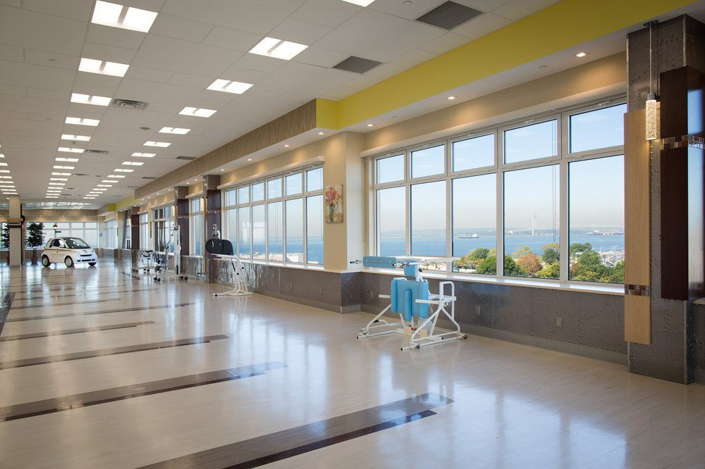 A bright, modern hospital corridor with large windows and seating areas.