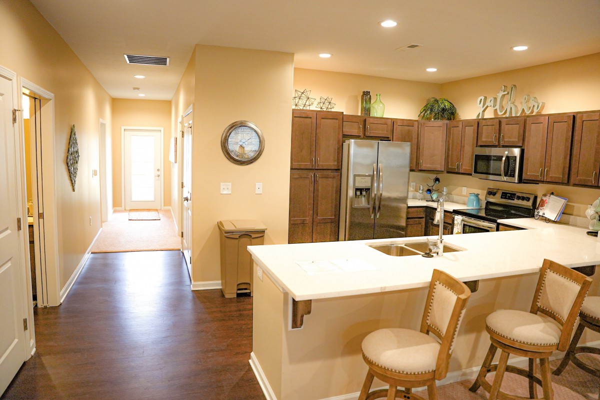 A modern kitchen interior featuring wooden cabinets and stainless steel appliances, complete with an island counter and bar stool.
