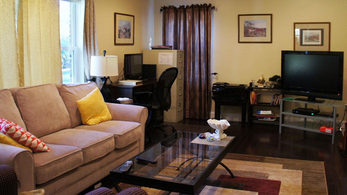 A cozy living room with a home office setup, featuring a sofa, coffee table, and desk with a computer.