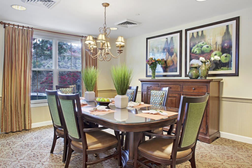 A beautifully decorated dining room featuring a wooden table, chairs with green accents, a chandelier, and artwork on the walls.