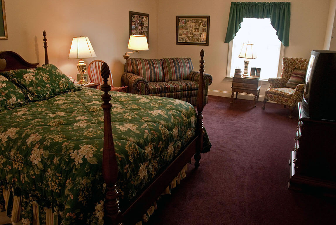 A cozy vintage-style bedroom with a floral bedspread, sofa, and warm lighting.