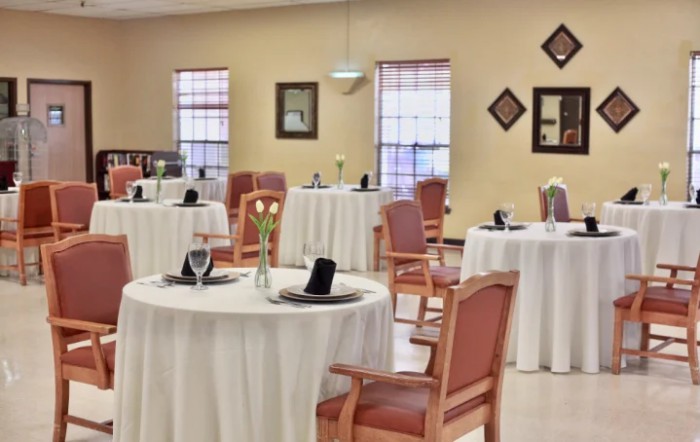 A neatly arranged dining room with round tables and wooden chairs.