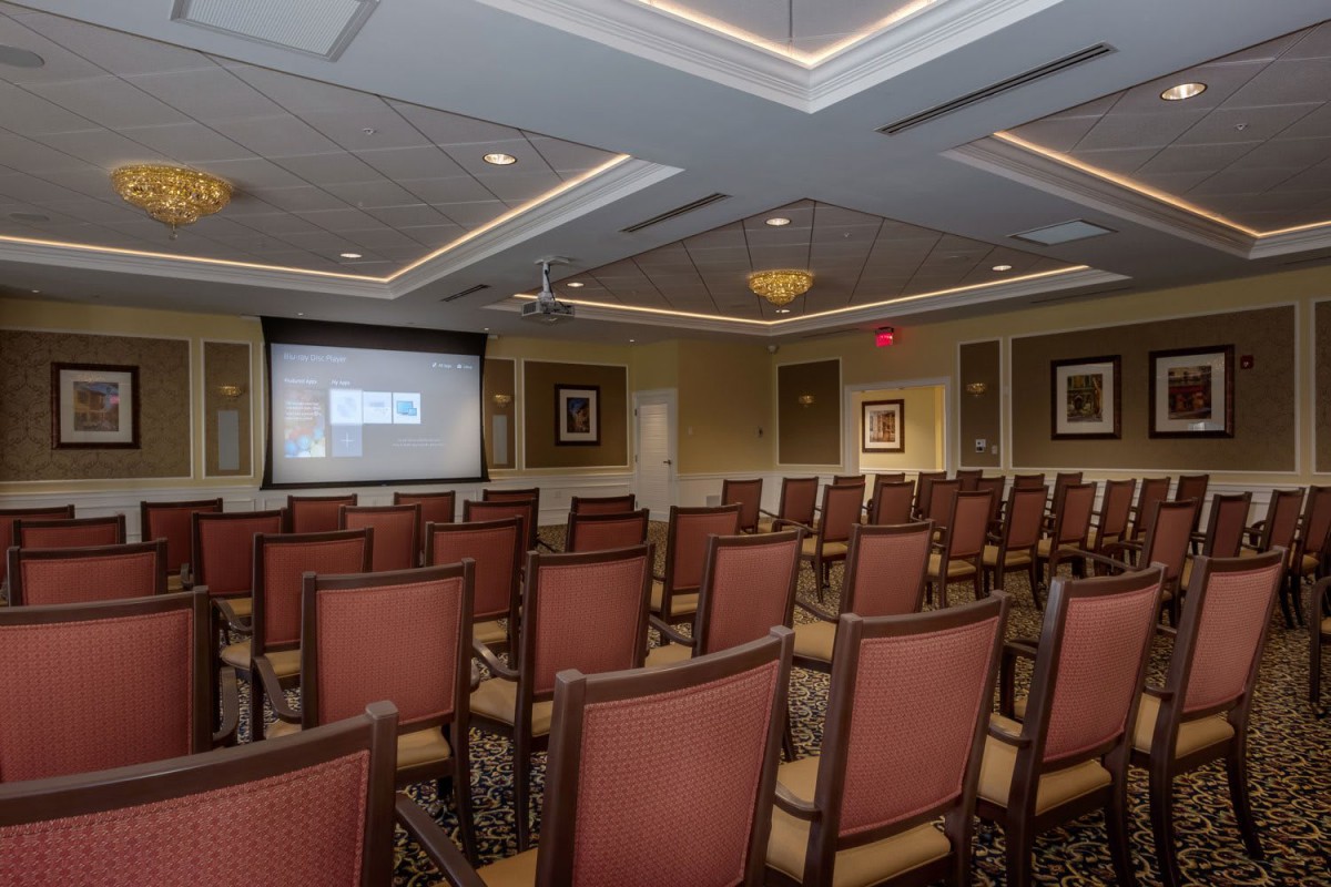 An empty conference room with rows of chairs facing a projector screen.