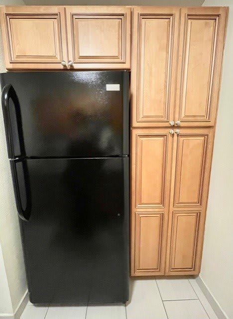 A black refrigerator next to wooden kitchen cabinets.