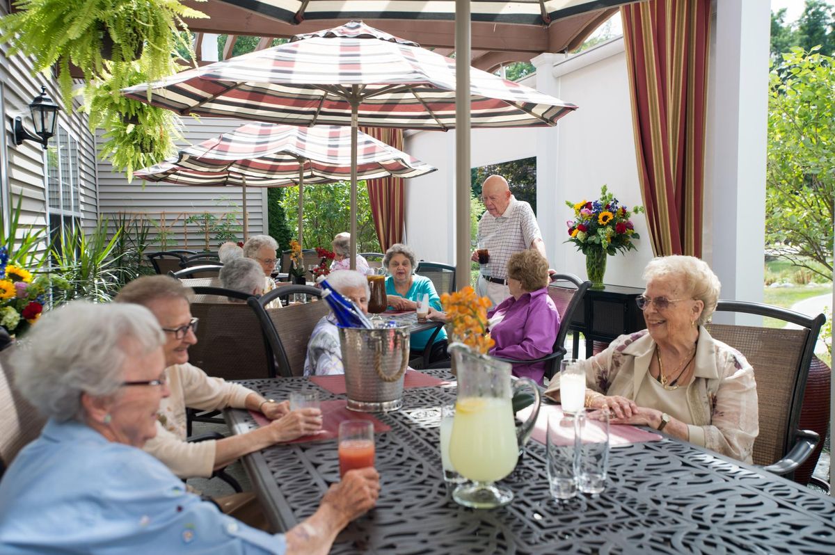 A group of elderly people enjoying a social gathering outdoors under patio umbrellas.