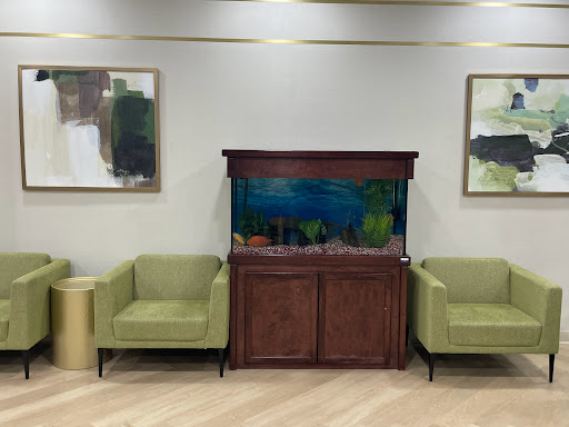 A cozy waiting area featuring green chairs and an aquarium, complemented by abstract art on the walls.