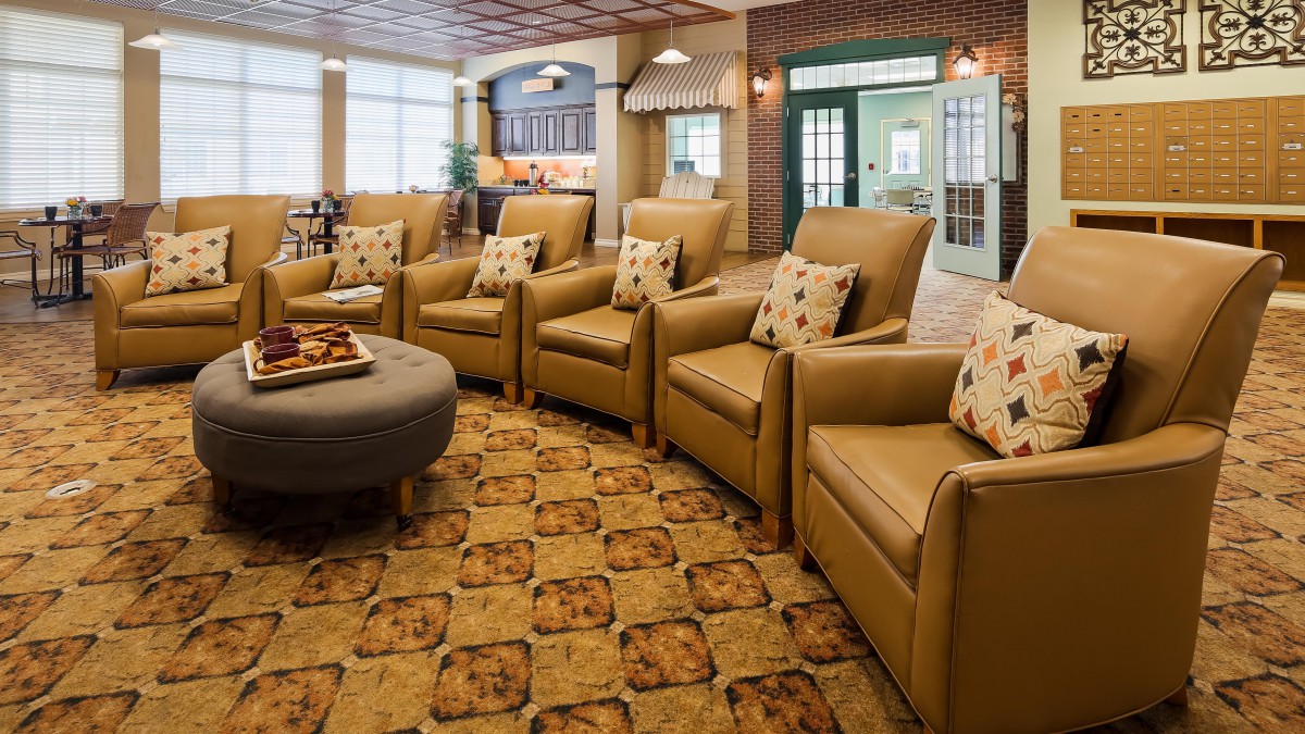 A cozy seating area with a circular arrangement of comfortable chairs and decorative pillows, set on a patterned carpet in a warm, inviting living room.