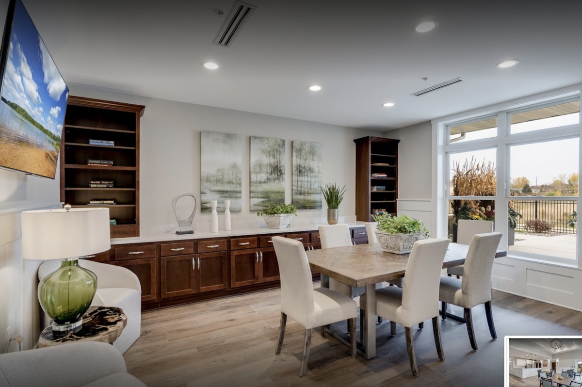 A modern dining room with a wooden table, white chairs, and built-in bookshelves.