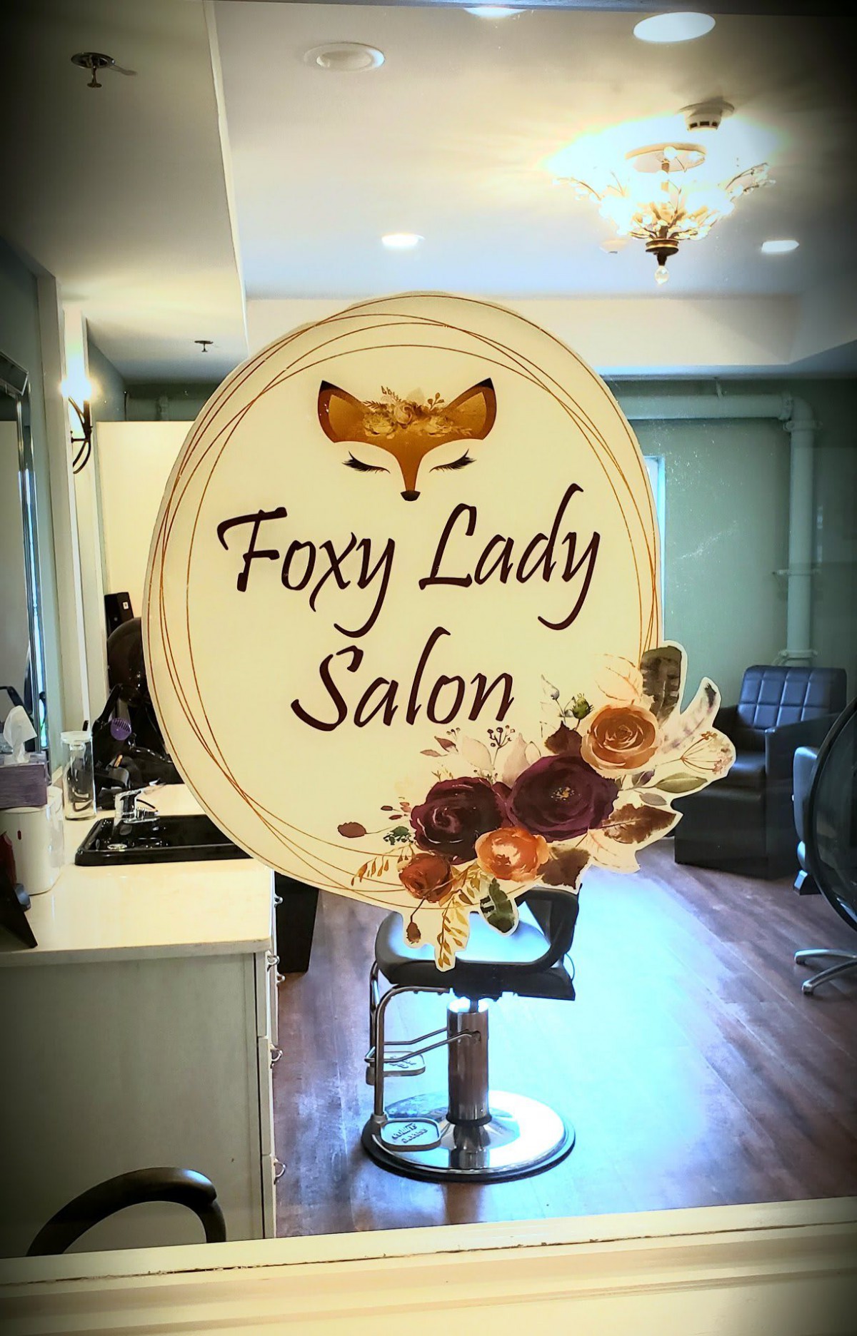 A stylish sign for 'Foxy Lady Salon' featuring a fox logo and floral decorations, displayed inside the salon.
