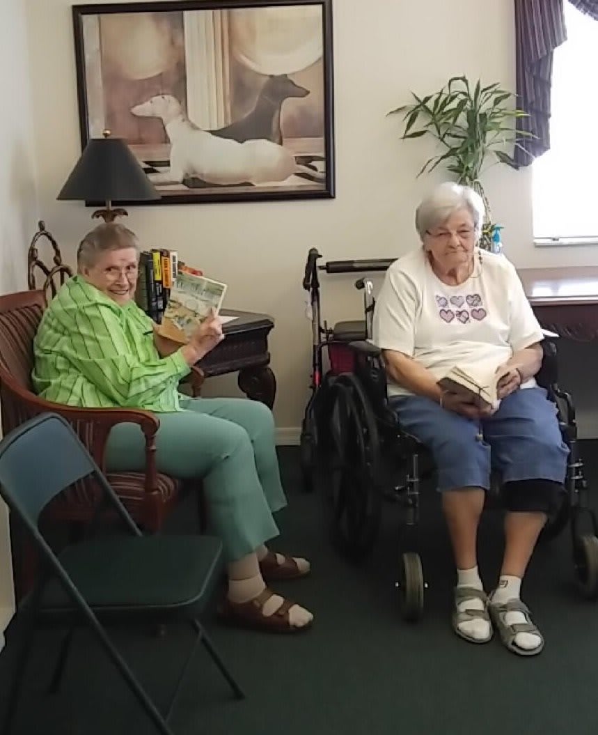 Two elderly individuals enjoying reading indoors, with one sitting in a wheelchair.