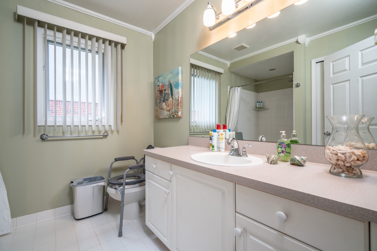 A well-lit bathroom featuring a spacious vanity, mirror, and natural light from the window with blinds.
