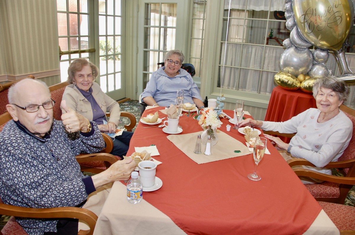 A group of seniors enjoying a meal together, seated around a decorated table indoors.