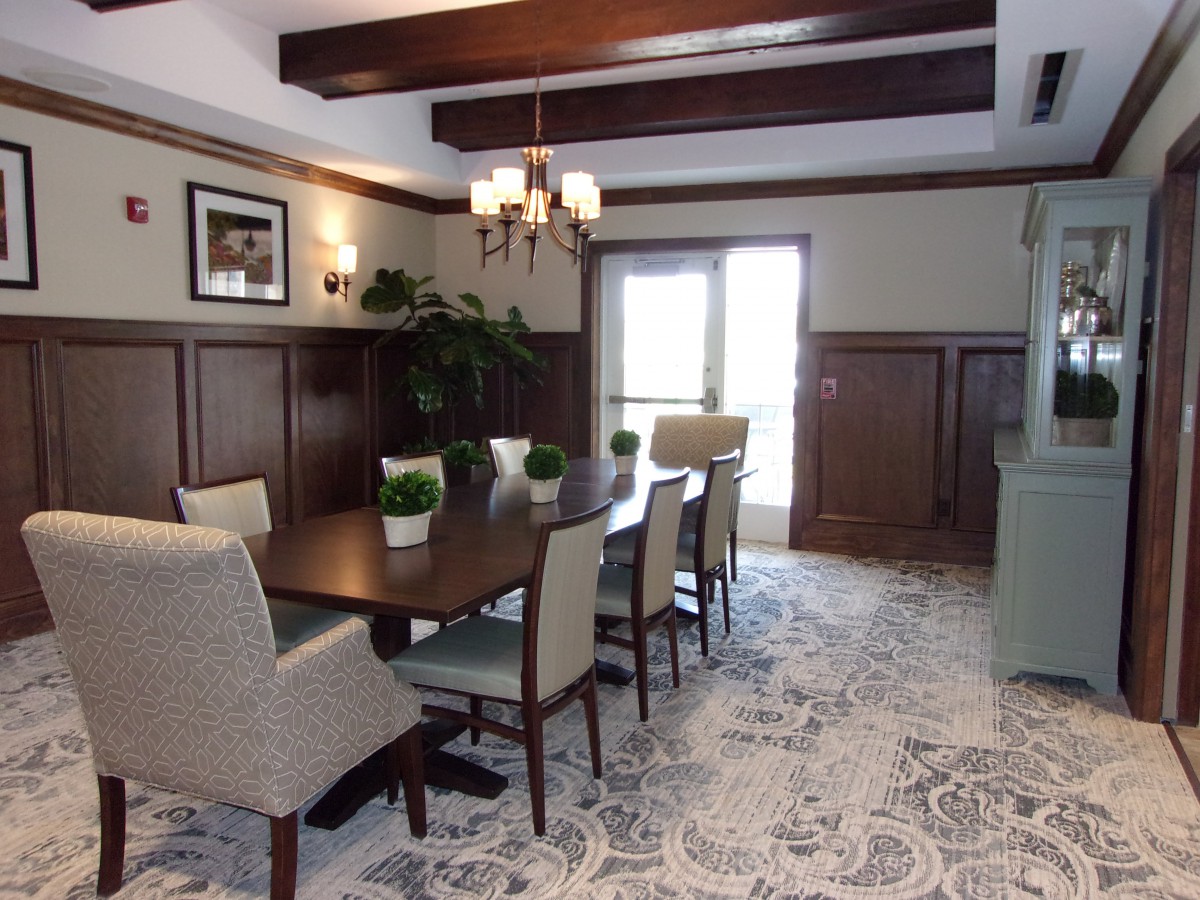 A well-appointed dining room featuring a rectangular table, upholstered chairs, wooden ceiling beams, and decorative plants.