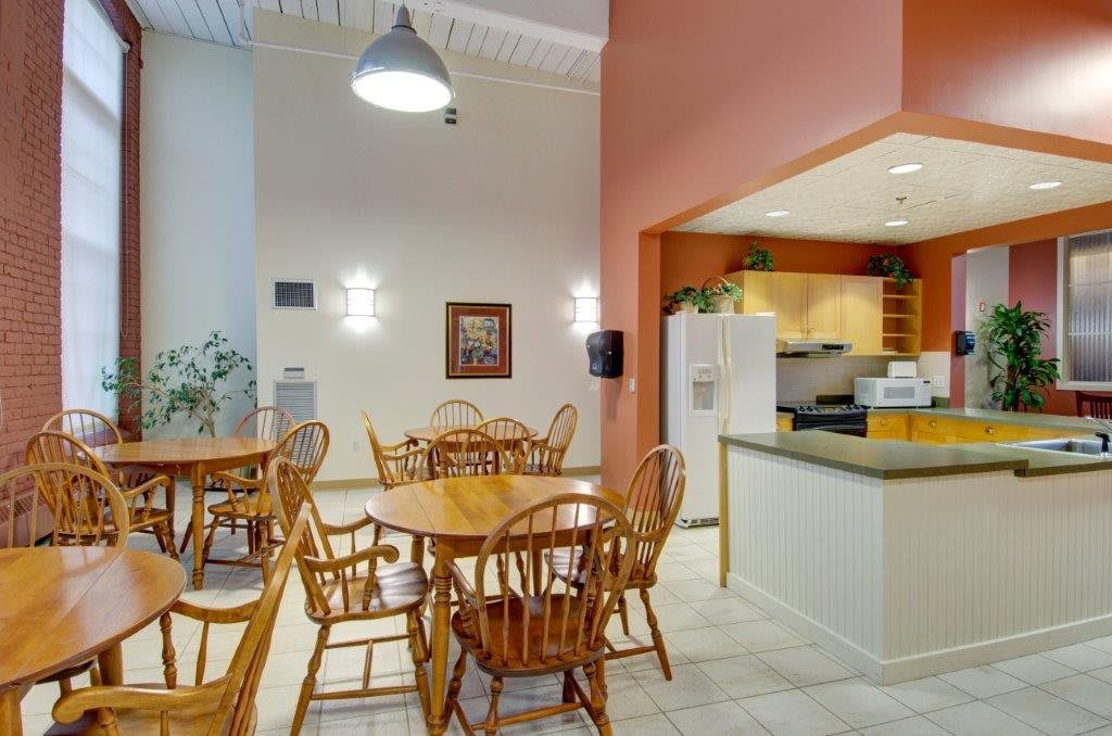 A cozy dining area featuring wooden tables and chairs adjacent to a small kitchen space.