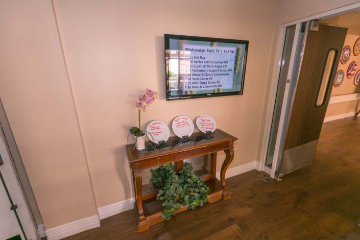 A cozy interior setup featuring a wooden table with decorative plates, an orchid, and a wall-mounted TV screen.