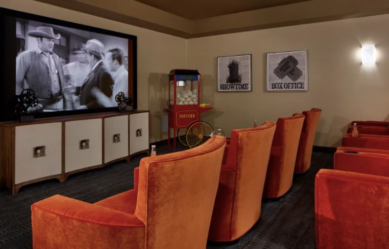 A cozy home theater with plush orange seating and a large movie screen, complete with a classic popcorn machine.