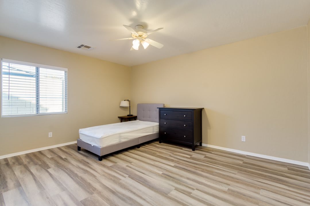 A simple bedroom with a mattress, dresser, and lamp on hardwood flooring.