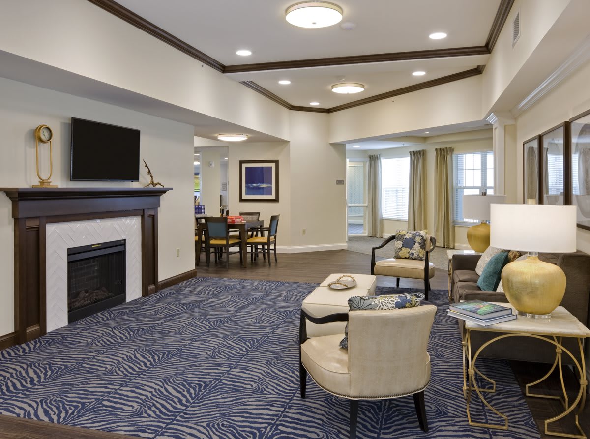 A spacious living room with a fireplace and modern furnishings, featuring a cozy seating area and a dining table in the background.