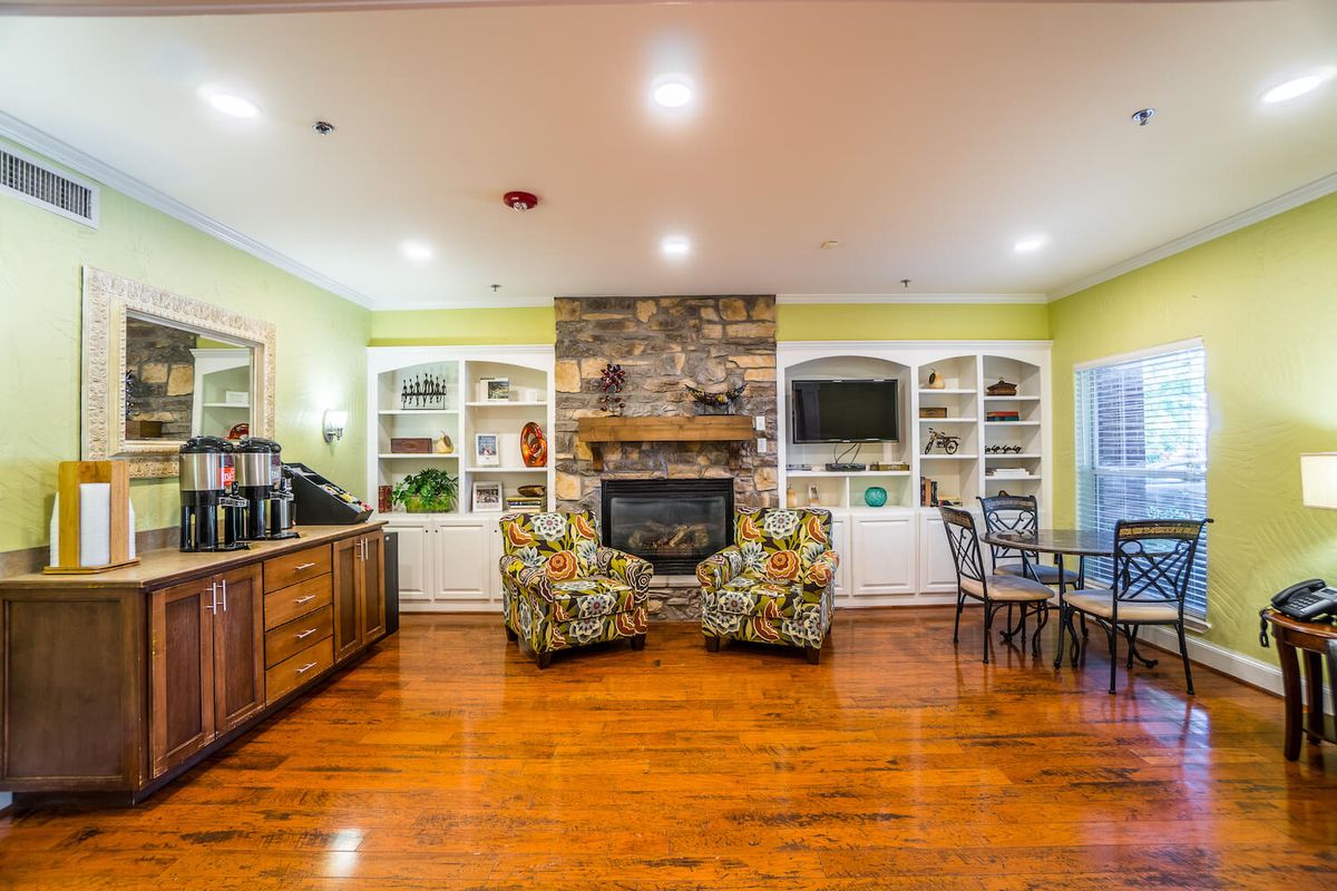 A cozy living room with a stone fireplace, built-in shelves, and vibrant chairs on hardwood flooring.