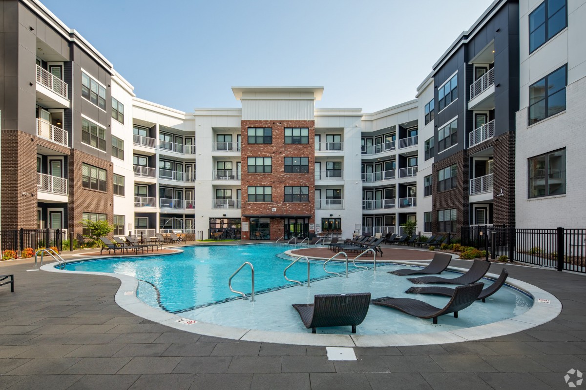 A modern apartment complex featuring a spacious swimming pool in the central courtyard.