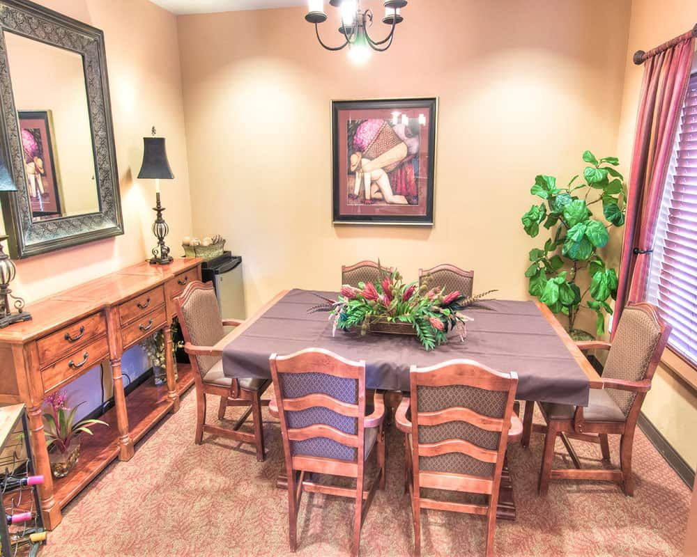 A cozy dining room with a wooden table and chairs, adorned with a central plant arrangement, surrounded by decor and wall art.