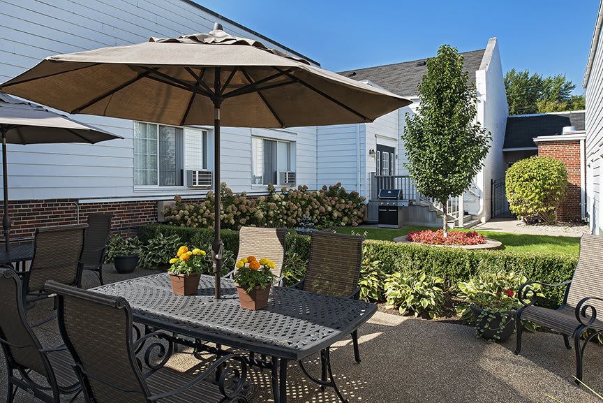 A cozy outdoor patio with a table, chairs, and an umbrella surrounded by a well-maintained garden.