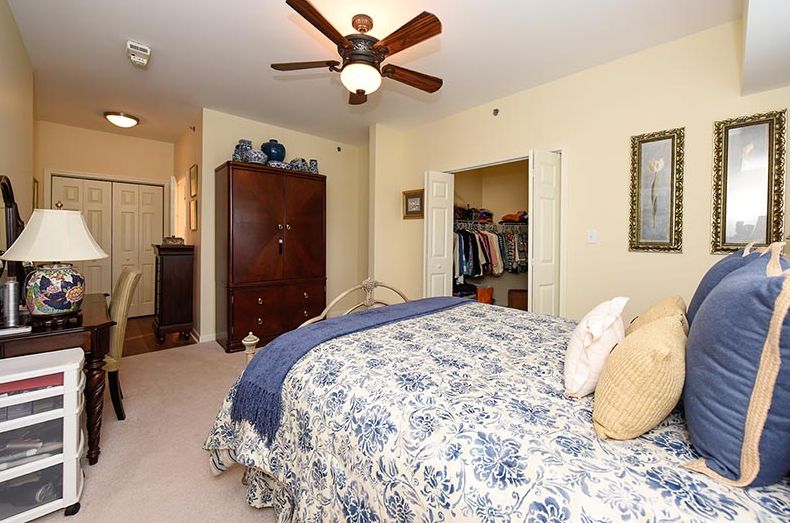 A cozy bedroom featuring a floral bedspread, ceiling fan, and an open closet.
