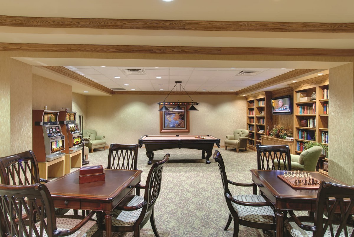 A cozy recreation room featuring a billiards table, wooden game tables, and comfortable seating.