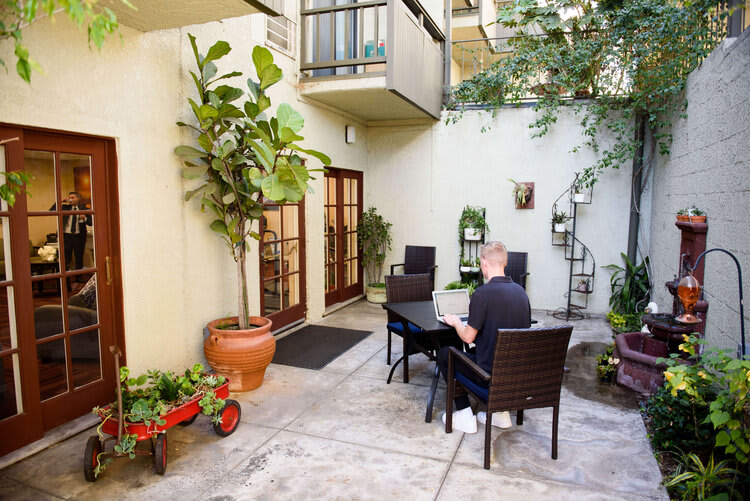 A serene courtyard with outdoor seating, potted plants, and a person sitting at a table.